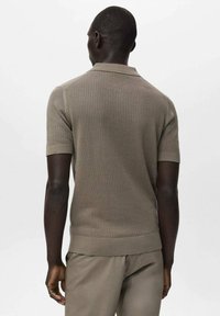 Polo a maniche corte in taupe con un motivo a maglia testurizzato, polsini a costine e colletto piatto, indossato da un modello visto di schiena.