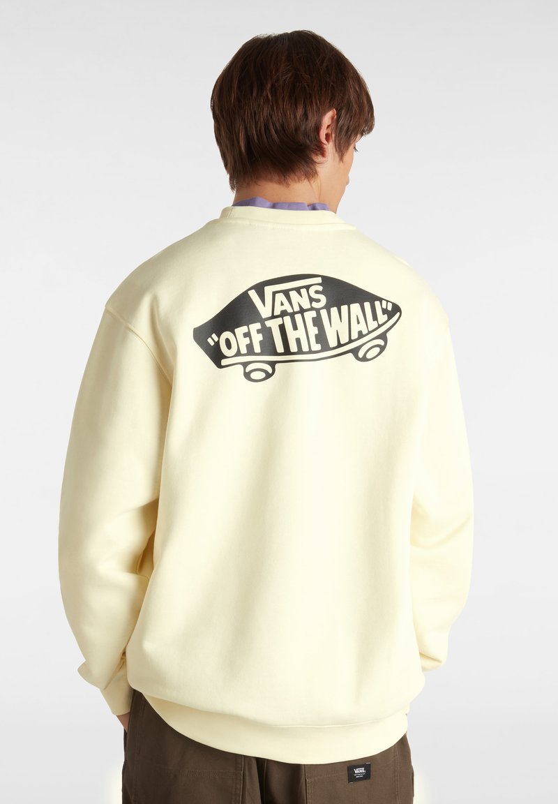 Gele Vans sweatshirt met een groot zwart "Off the Wall" graphic en skateboardontwerp op de achterkant, gemaakt van zacht materiaal.