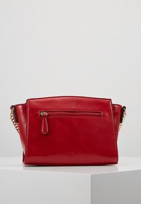 Borsa a tracolla in pelle rossa con un design strutturato, dotata di una tasca frontale con zip, dettagli in catena dorata e una texture liscia.