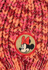 Gestrickte Mütze in Rosa- und Orangetönen mit goldenen Fäden. Sie hat einen runden Aufnäher mit einer Cartoonfigur und einer roten Schleife.