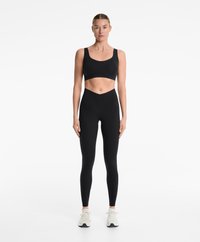 Soutien-gorge de sport noir et leggings taille haute en tissu lisse et extensible. Les chaussures sont blanches avec des accents texturés et des lacets.