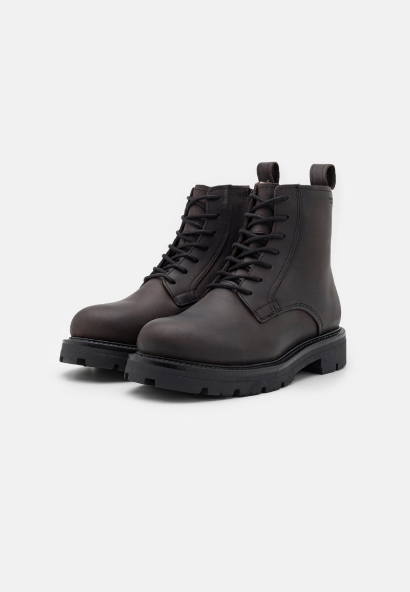 Brązowe skórzane botki sięgające kostki z zapięciem na sznurówki, okrągłym noskiem i teksturowaną gumową podeszwą z płaskim obcasem. Pętla z tyłu ułatwiająca zakładanie.