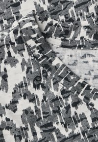 Katoenen stof in wit, grijs en zwart met een abstract patroon. Heeft een zachte textuur en een ronde halslijn met afgewerkte randen.