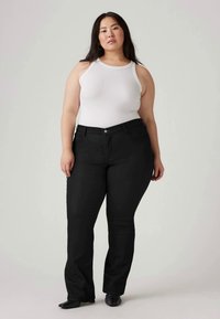 Black denim pants with a slight flare, featuring a classic five-pocket design and a visible front button closure, paired with a white tank top.