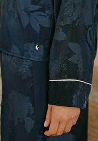 Navy fabric pajama set featuring a floral pattern, with a light pink accent on the cuff and a small silver logo detail.