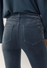 Mörkblå kordfläskbyxor med bakfickor bärs av en person i en matchande mörk överdel, visad från midjan till låren.