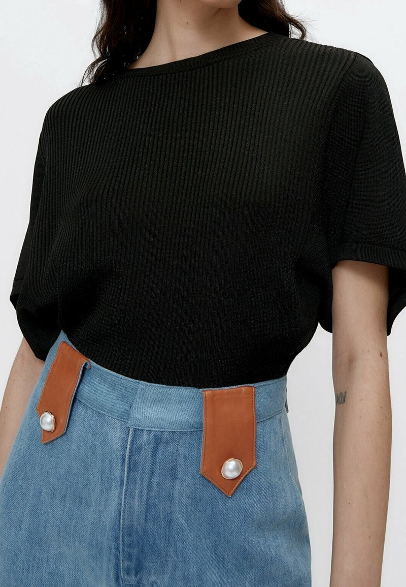 Sort kortærmet ribstrikket top kombineret med højtaljede lyseblå jeans med tan-accenter og store perleknapper.