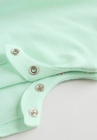 Svetlozelená látka s kovovými cvokmi, čiastočne otvorená, odhaľujúca textúrovaný pletený materiál a detaily švov.