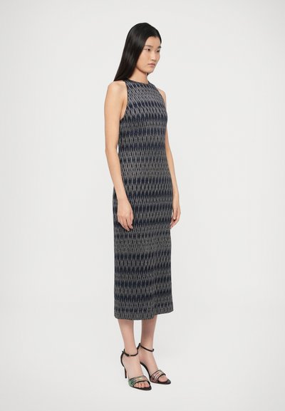 Bespalvė, figūrą pabrėžianti suknelė iš tekstūruotos medžiagos su geometriniu raštu tamsiai mėlynos ir pilkos spalvų. Modelis derina su daugių spalvų kulniukais sandalais.