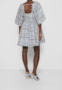 Kortärmad mönstrad klänning i blått och vitt med en utskärning i ryggen. Tyget har en strukturerad design. Matchas med ljusblå högklackade sandaler.