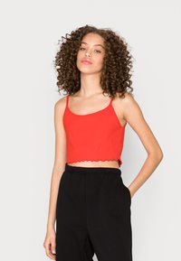 Top cropped vermelho com nervuras e bainha ondulada, combinado com calças pretas de cintura alta. Tecido com textura suave, ajuste casual.