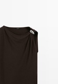Robe sans manches marron foncé avec un décolleté drapé, ornée d'un accent argenté à l'épaule. Fabriquée en tissu doux et lisse.