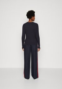 Maglione a coste navy con maniche lunghe abbinato a pantaloni wide-leg navy con strisce laterali bianche e rosse. Texture liscia, vestibilità informale.