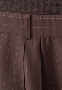 Gros plan sur un tissu marron à fines rayures avec des plis et une passants de ceinture cousu sur une ceinture.
