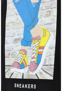 Zapatillas coloridas con secciones azules, amarillas y rosas, con acentos de tachuelas y cordones blancos, exhibidas contra un fondo de ladrillo.