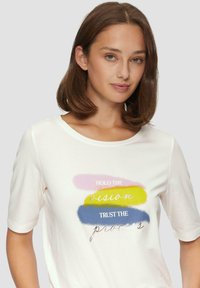T-shirt blanc à manches courtes avec des graphiques textuels multicolores : rose, jaune, bleu. Tissu doux avec un col rond et une coupe décontractée.