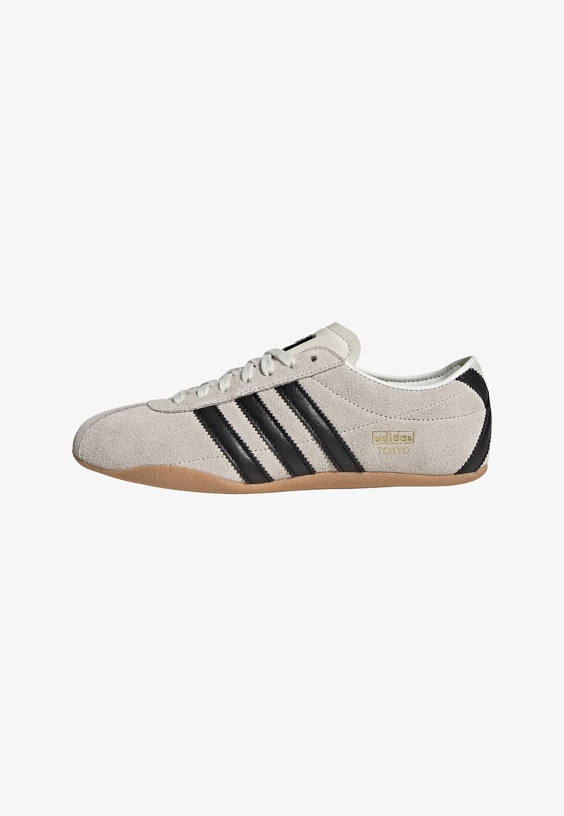 Sneaker in suede grigio con strisce in pelle nera, dettagli bianchi e suola in gomma. Presenta lacci rotondi e logo del marchio sul lato.