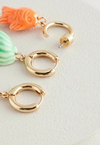 Guldtonede hoops med farverige fiske- og skaldyrscharmes, med glatte overflader og en poleret finish. Teksturerede detaljer er synlige.