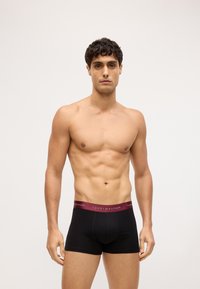 Boxer shorts negros con una cinturilla burdeos de Tommy Hilfiger. Hechos de un material suave, diseño ceñido y textura lisa.