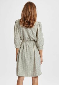 Abito a scacchi con vita aderente, maniche a palloncino e orlo di lunghezza media; realizzato in tessuto leggero nelle tonalità neutre del beige e del nero.