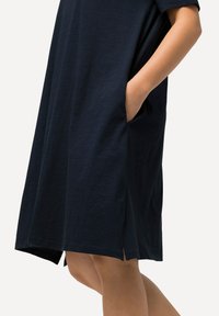Námořnické modré bavlněné šaty s krátkými rukávy, bočními kapsami a volným střihem. Mají mírný asymetrický lem a hladkou texturu.