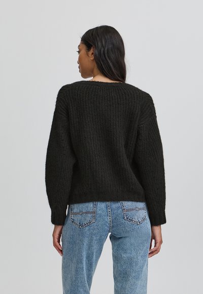 Pulover negru tricotat cu textură în relief, mâneci largi și decolteu rotund, asortat cu blugi din denim de un albastru deschis.