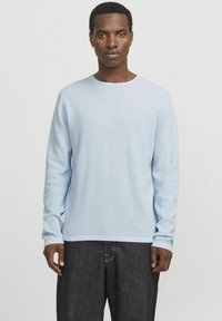Suéter de manga larga azul claro con un patrón texturizado, cuello redondo y puños acanalados. Unos jeans oscuros completan el look.