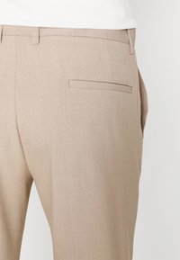 Pantaloni beige su misura realizzati in tessuto liscio con taglio aderente, caratterizzati da una tasca posteriore e un design frontale piatto.
