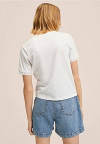 Camiseta blanca corta de manga corta con detalle de encaje en los puños, combinada con pantalones cortos de mezclilla azul claro que tienen bolsillos traseros.
