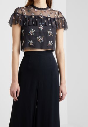 Crop top noir transparent avec manches volantées et broderie florale multicolore, associé à un pantalon noir large taille haute.