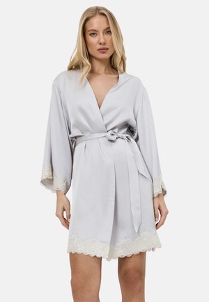 Femme blonde portant une robe en satin gris clair avec une bordure en dentelle aux manches et à l'ourlet, nouée à la taille avec une ceinture.
