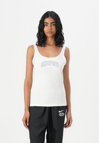 Hvit tank topp med rund hals og tynne stropper, med en "NIKE SPORTS" grafikk i lilla over brystet. Glatt tekstur.