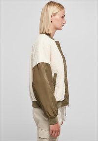 Bomber bunda s telom z krémového fleecu a rukávmi z olivovo zelenej nylonu. Obsahuje predný zips, elastické manžety a uvoľnený strih.