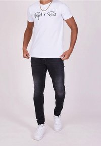 Camiseta blanca con texto en cursiva negra que dice "Project x Paris", combinada con jeans oscuros ajustados y zapatillas blancas. Diseño simple y casual.