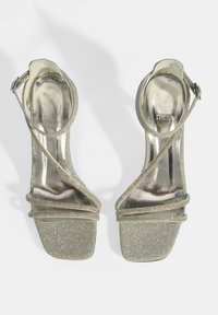 Strap sandalen met hoge hak in licht zilver met glinsterende textuur, vierkante neus en enkelgesp. Voorzien van dunne banden en metallic accenten.