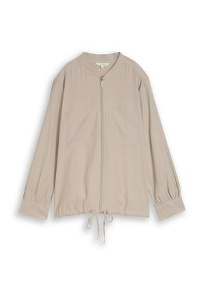 Veste beige à manches longues avec fermeture éclair frontale, deux poches poitrine, poignets froncés et ourlet réglable à cordon de serrage.