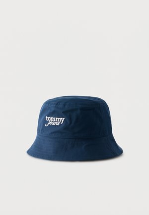 Granatowy kapelusz typu bucket z białym, wyszywanym logo "tommy jeans" z przodu, wykonany z bawełnianej tkaniny, z przeszywanym rondem na jednolitym jasnym tle.