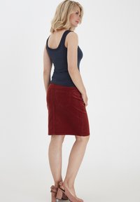 Canotta blu abbinata a una gonna di velluto a coste rossa lunghezza ginocchio con tasche sul retro, completata da scarpe con tacco rosa con fiocchi.