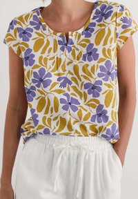 Top corto a maniche corte con motivo floreale bianco, caratterizzato da fiori viola e foglie gialle. Presenta un colletto a girocollo e piccoli dettagli sul davanti.