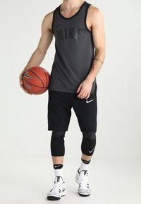 Completo sportivo Nike composto da un top smanicato nero con logo in rilievo, pantaloni corti neri, tutori neri per le ginocchia e scarpe da ginnastica bianche con suola decorata.