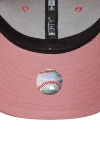 Baseballpet van zacht roze stof met een zwarte klep. Bevat een zilveren MLB-sticker met rode stikdetails en een gestructureerde binnenvoering.