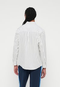 Bela srajca z mornarsko modrimi vertikalnimi črtami, dolgi rokavi, ovratnik z gumbi, ukrivljen rob in manšete z enim gumbom. Oblika slim fit.
