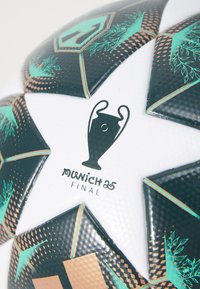 Fotboll med en vit yta med svarta och turkosa geometriska mönster, koppardetaljer och design av UEFA Champions League-trofén.