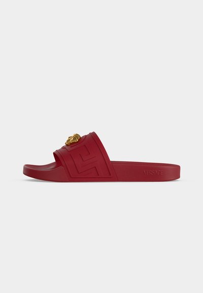Sandale mule rouge avec motif clé grec en relief, emblème tête de Méduse dorée sur la bride, et semelle texturée avec le logo "Versace" sur le côté.