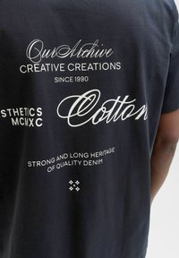 Schwarzes Baumwoll-T-Shirt mit weißem Text. Designs umfassen "Unser Archiv", "Kreative Kreationen" und Blumenmotive. Lässige Passform.