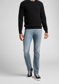 Schwarzer gestrickter Langarmpullover mit rundem Ausschnitt, getragen über hellblauen Jeans und schwarzen High-Top-Sneakern mit weißen Schnürsenkeln.
