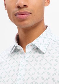 Camicia bianca con motivo a foglia color verde menta, design con bottoni e colletto a punta. Tessuto testurizzato con un sottile motivo geometrico.