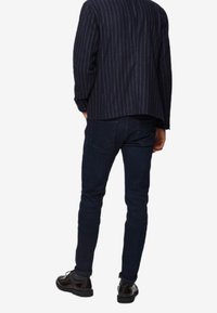 Blazer de rayas marineras con un corte relajado, combinado con jeans ajustados azul oscuro y zapatos negros, visto desde la parte trasera.