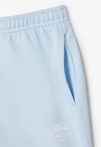 Pantaloni sportivi azzurri chiari realizzati in morbido tessuto, con vita elastica, tasche laterali e un piccolo logo Lacoste bianco.