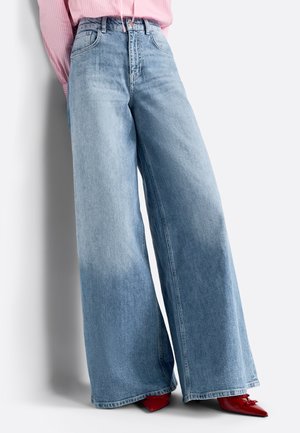 Jeans de tiro alto en denim de color azul claro y corte ancho, con un ligero desgaste. Combinados con zapatos rojos de punta visibles en la parte inferior.